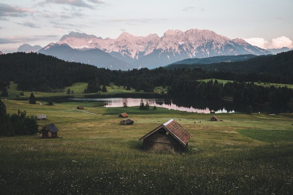 landscape photo of green fields with some small houses, lake and mountain in the back